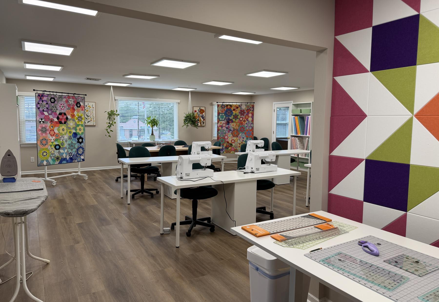 Inside The Sew Happy Studio: white worktables, Baby Lock sewing machines, and the colorful quilt-block accent wall
