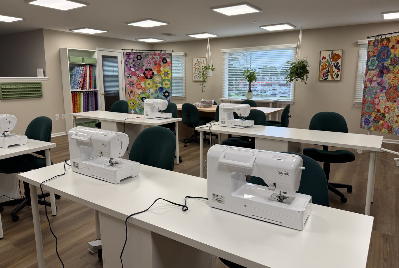Rows of Baby Lock machines on white tables beneath colorful hexagon quilts