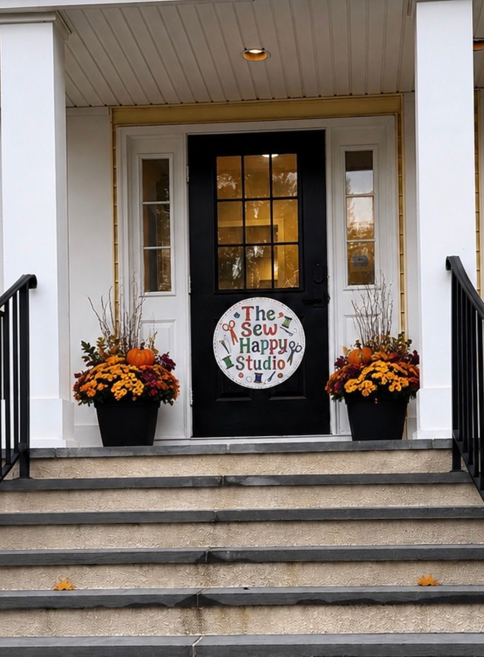 The Sew Happy Studio entrance with the logo on the door and fall planters on the steps